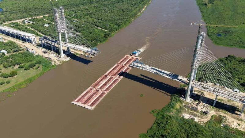 Comboio de chatas com minério de ferro passando sob a obra da ponte no Rio Paraguai, em Porto Murtinho